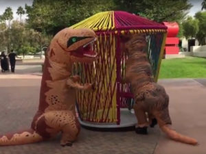two people in dinosaur costumes interacting with sculptures